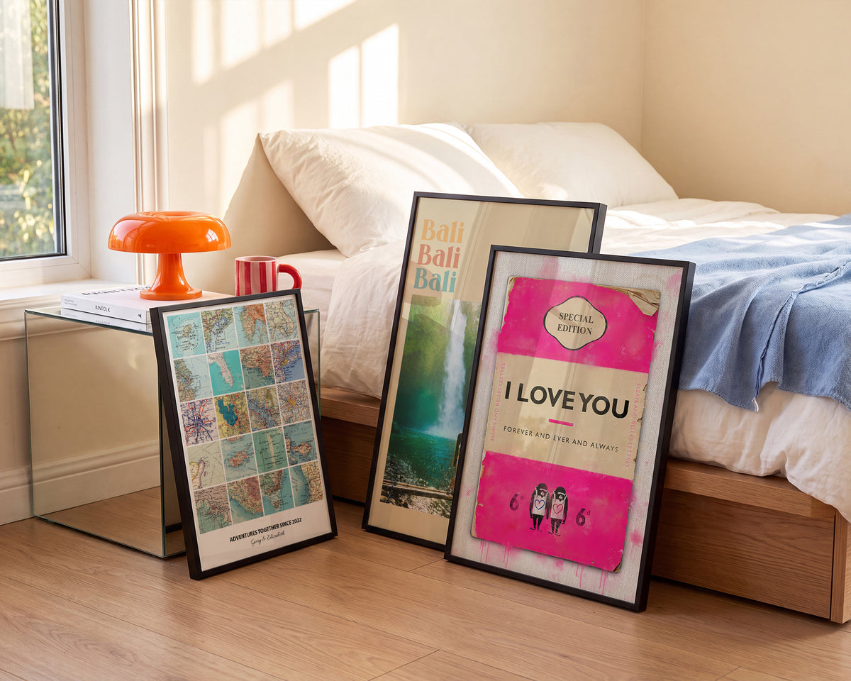 Three framed personalised prints, a photo collage, a Bali travel print and a pink I Love You book cover print, leaning against a bed