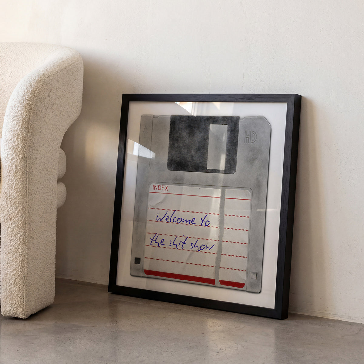 Framed personalised retro floppy disk print leaning against a wall beside a cream armchair