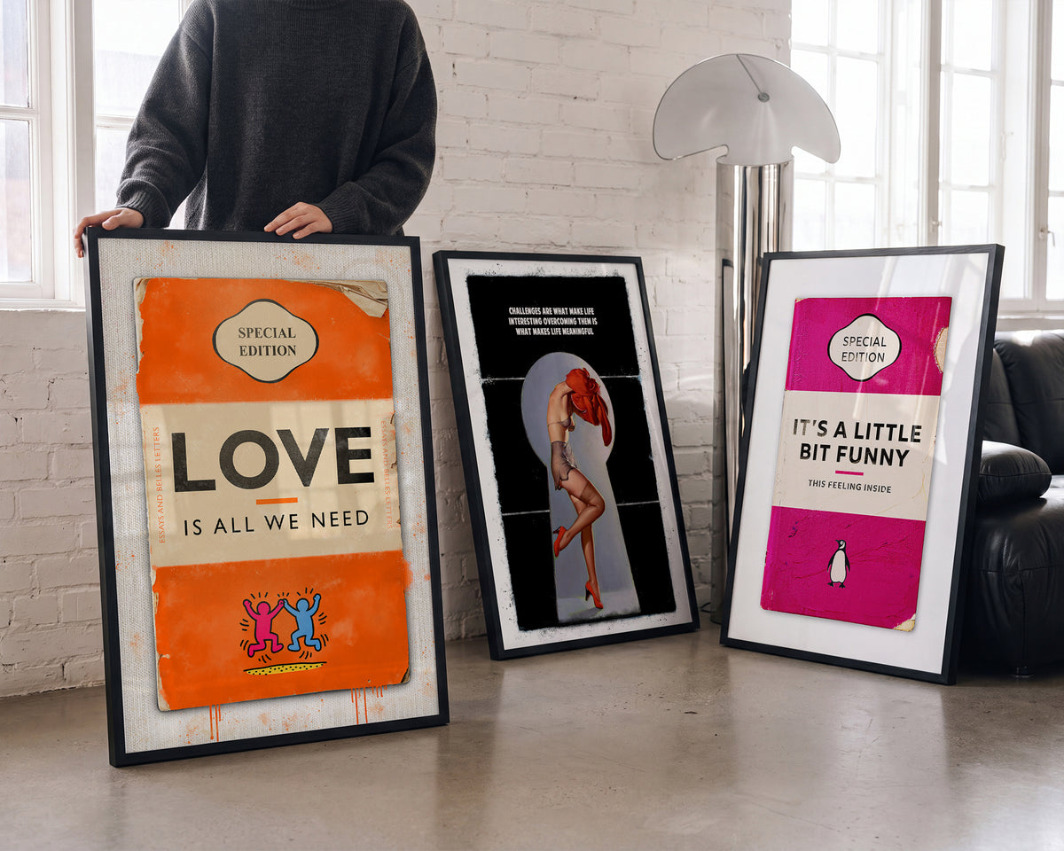 Limited edition book cover art prints, including Love Is All We Need, leaning against a white brick wall
