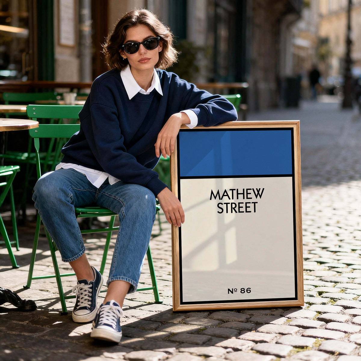 Man sitting outdoors next to a framed personalised street name print reading Mathew Street